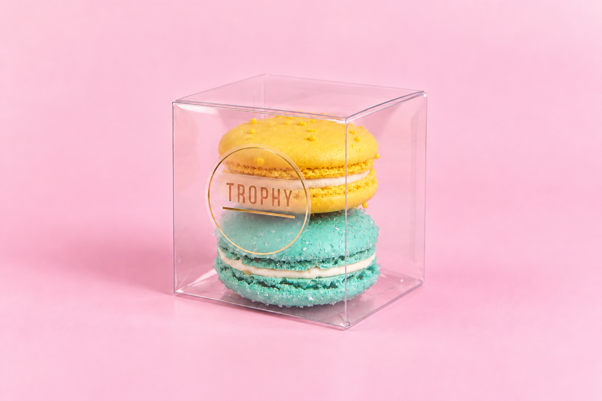 Two Trophy macarons, one yellow and one aqua, in a clear gift box with a round Trophy sticker