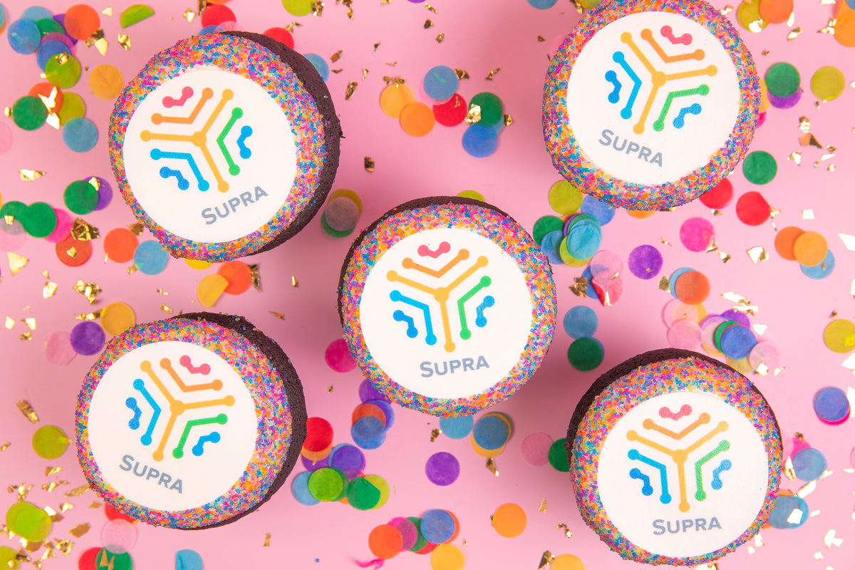 Five Trophy cupcakes topped with a full-color company logo, scattered with confetti