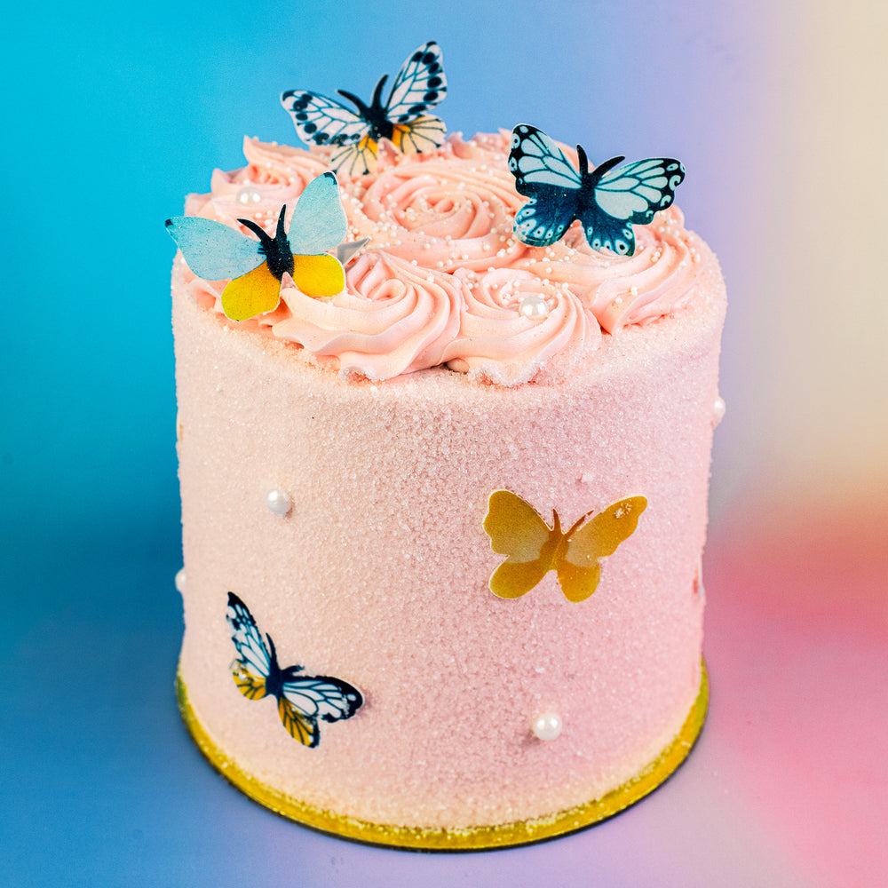 Beautiful Butterfly Cake with pink buttercream rosettes and edible butterflies on a gold cake board