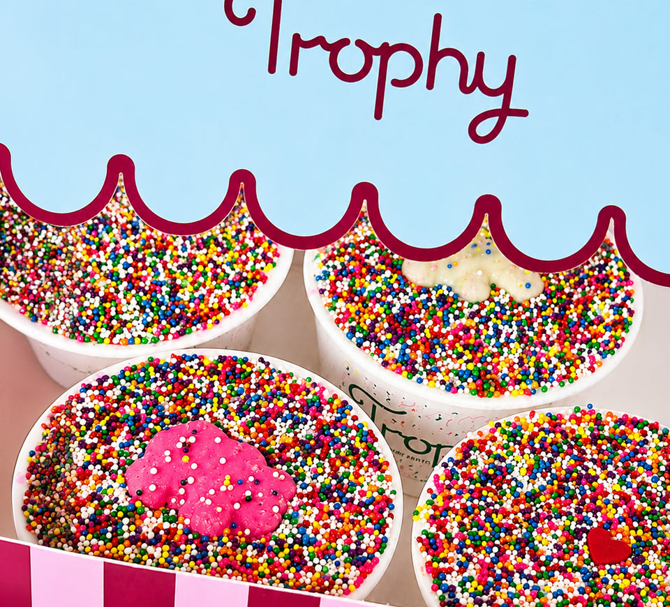Four Trophy Sprinkle Cake Cups packed beneath the scalloped lid of the striped Trophy box
