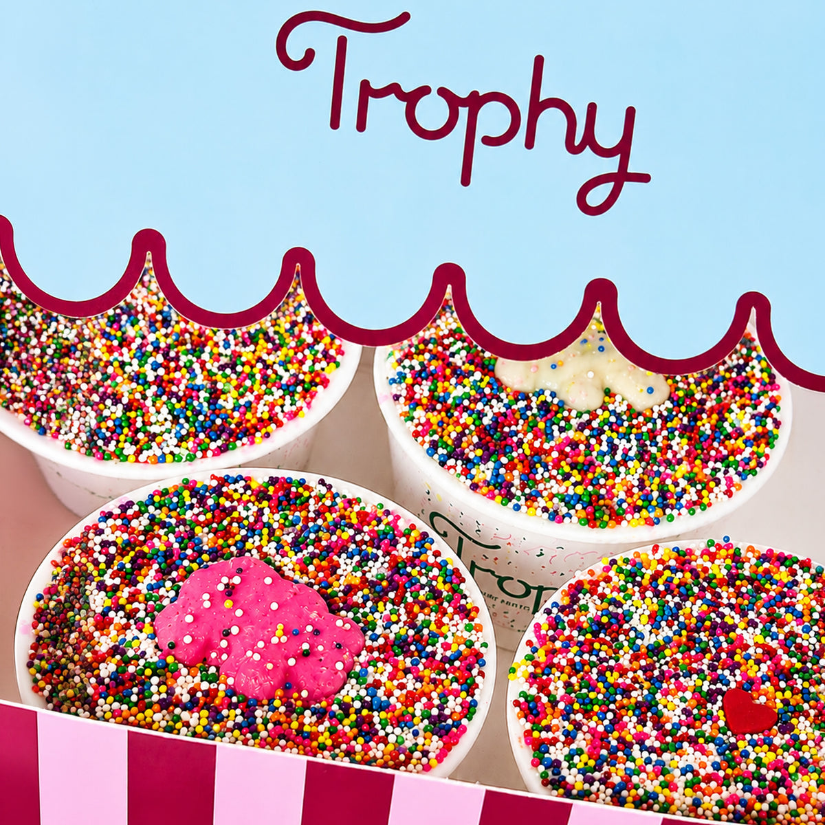 Four Trophy Sprinkle Cake Cups packed beneath the scalloped lid of the striped Trophy box