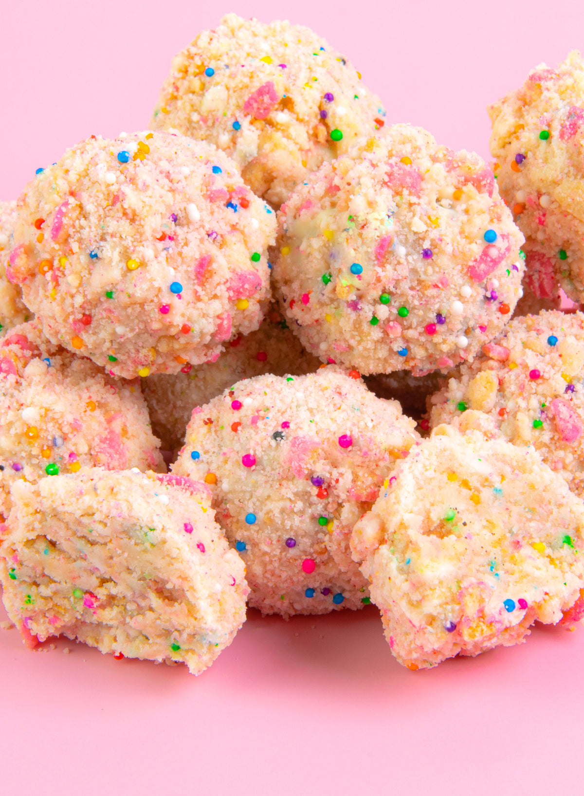Pile of cupcake truffles rolled in cake crumbs and rainbow sprinkles on a pink background