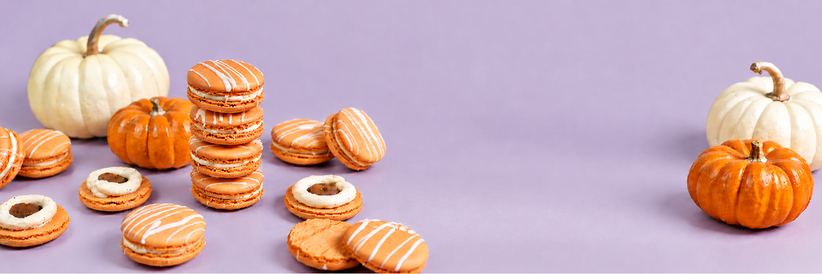 Orange macarons, a stack of four, with white and orange pumpkins on a lavender background