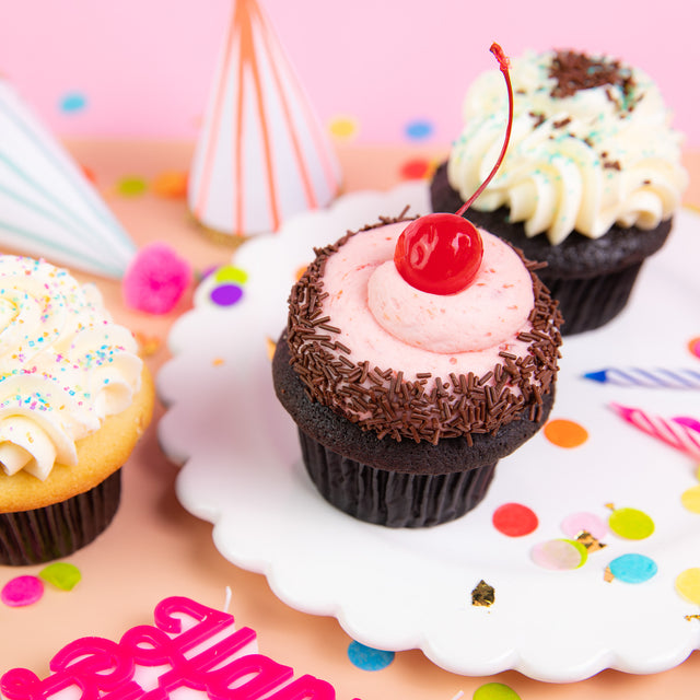 Birthday cupcakes with a cherry on top, party hats and confetti.