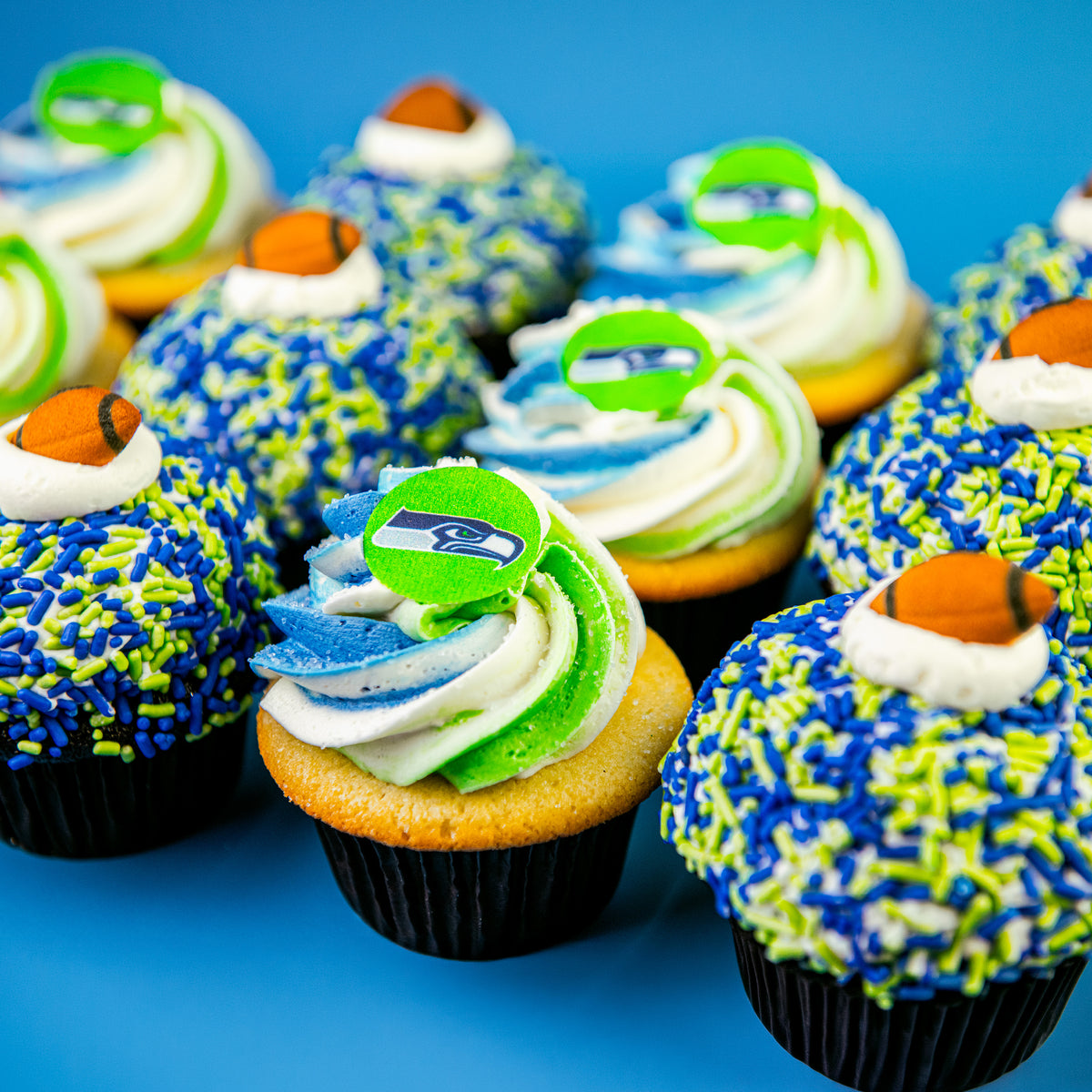 Close-up of blue and green sprinkle cupcakes with football toppers and blue, green and white swirled cupcakes with green team logo toppers