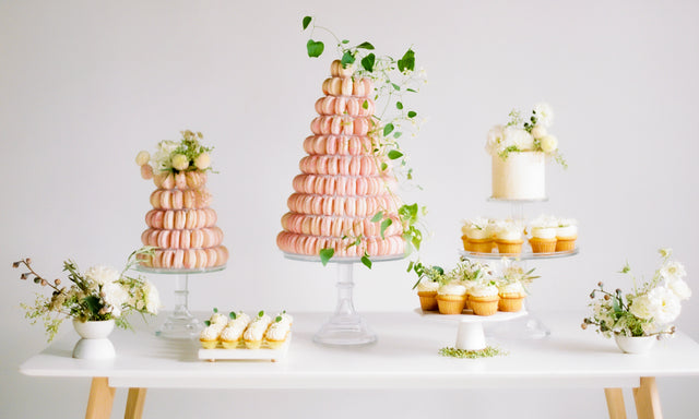 A wedding dessert table with macaron towers, small white cakes and cupcakes.