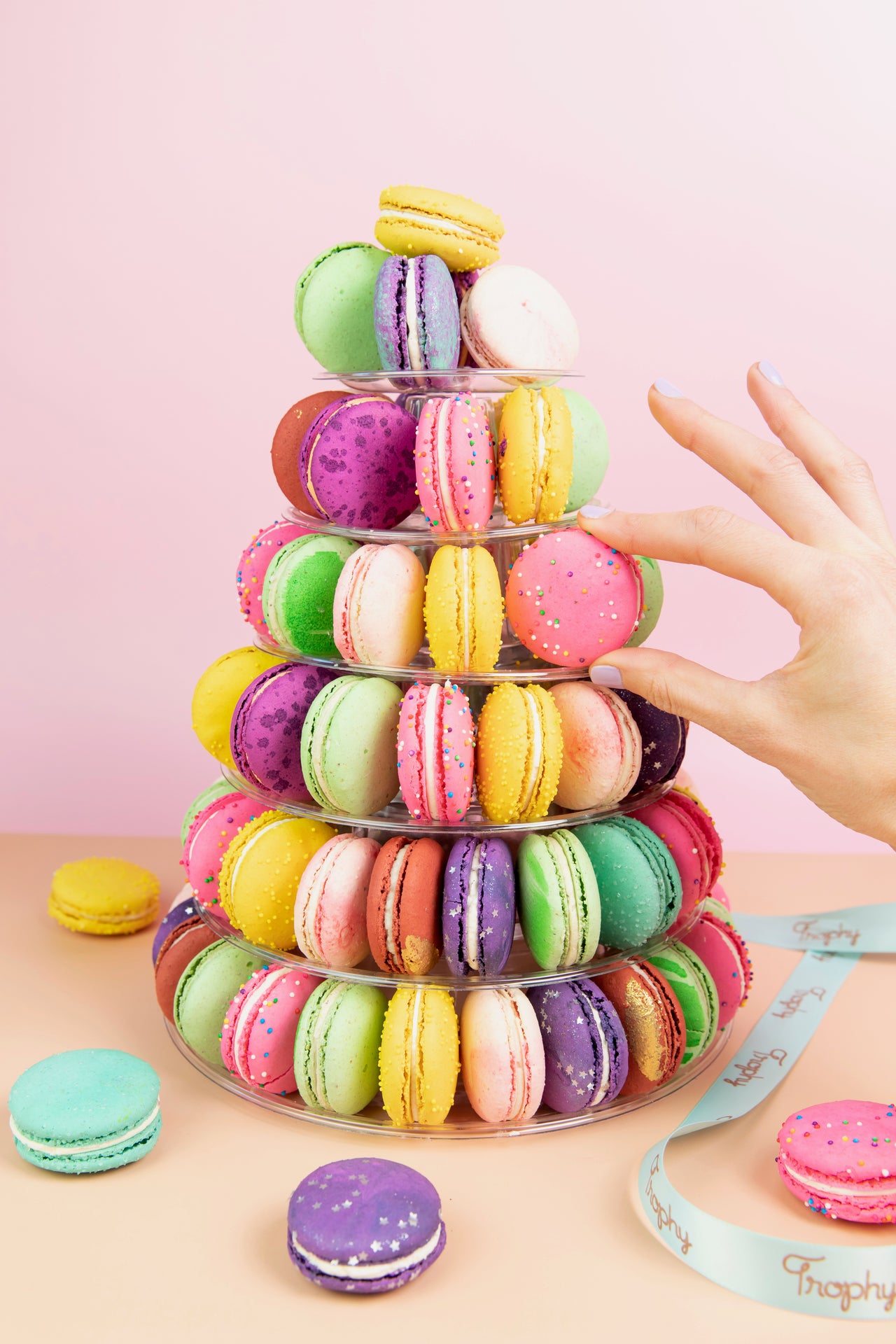 Six-tier Trophy macaron tower with a hand reaching for a pink macaron